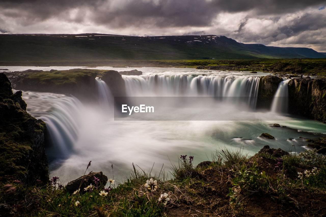Scenic view of waterfall against cloudy sky
