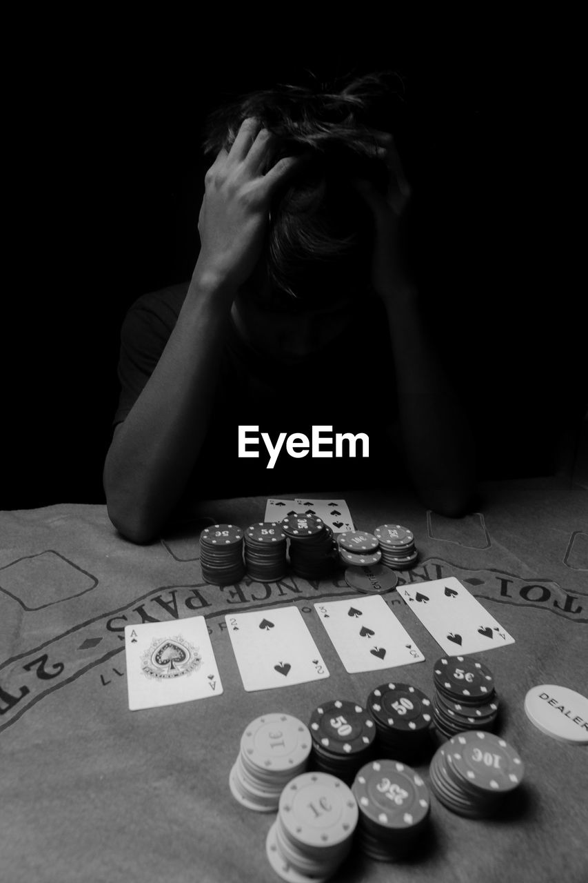 Man with head in hands gambling against black background