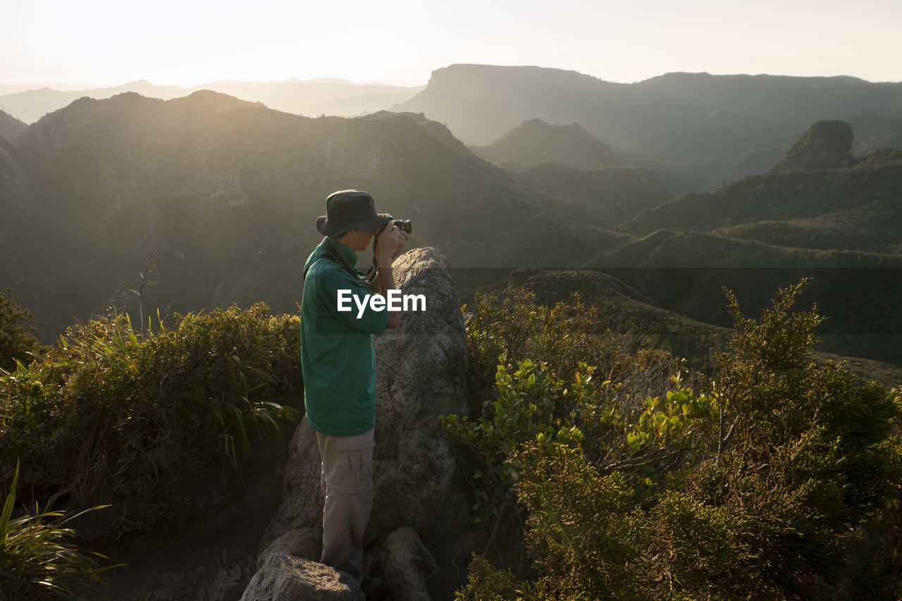 MAN STANDING BY MOUNTAINS AGAINST SKY