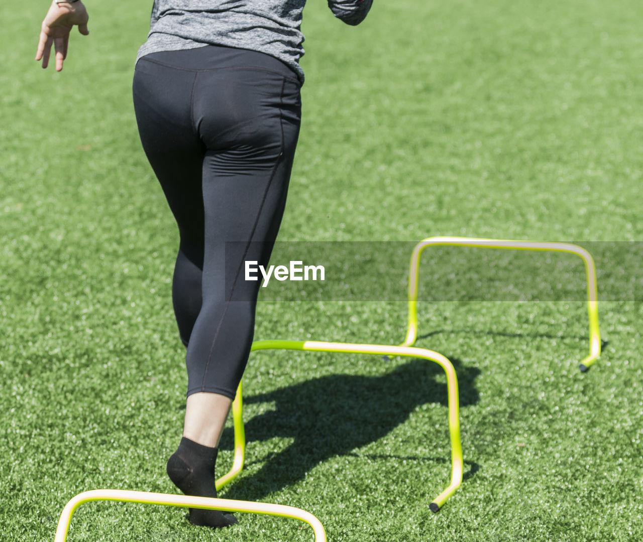 Rear view of woman running over hurdles on turf