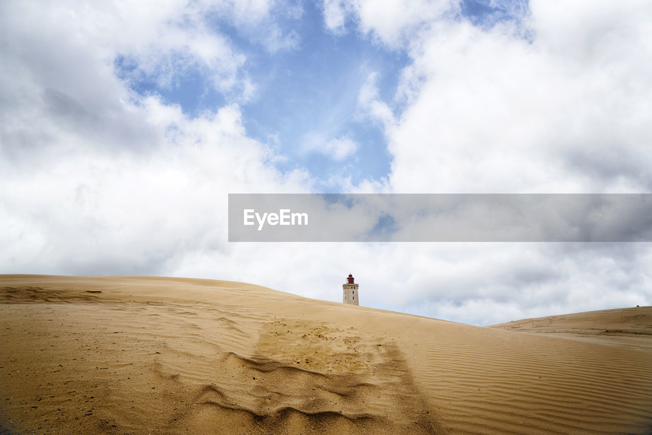 Low angel view of lighthouse over sand dunes against sky