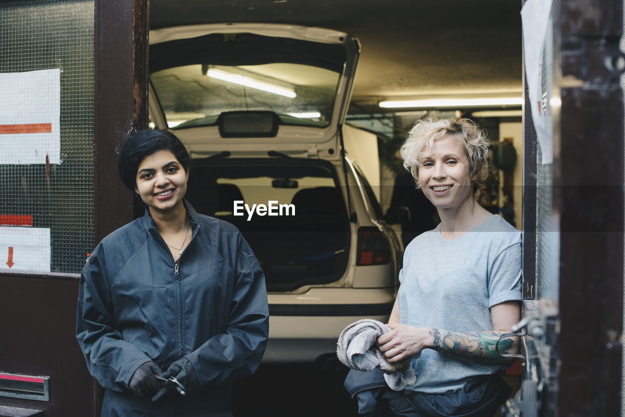 Portrait of female coworkers standing at entrance of auto repair shop