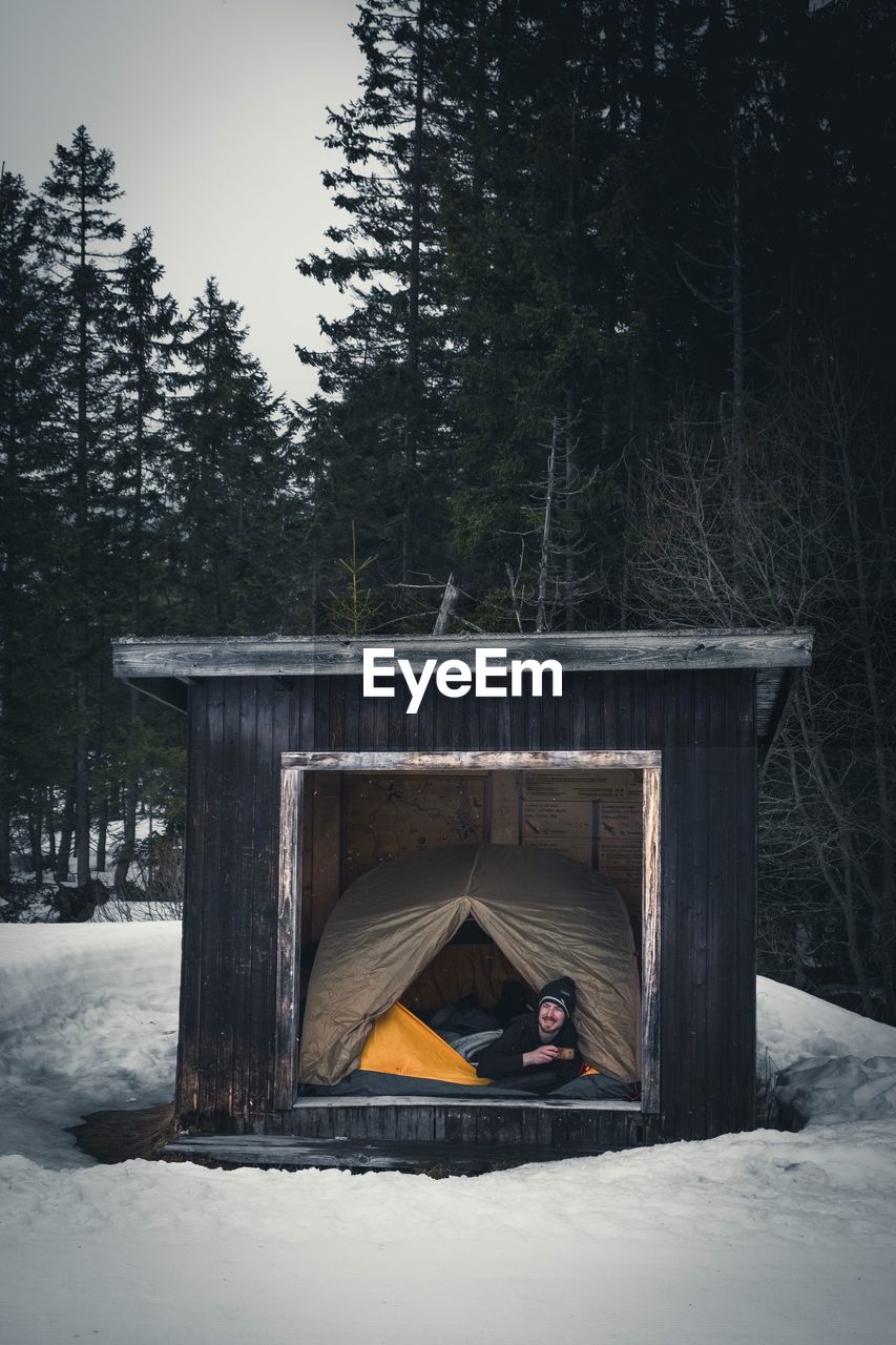 Young man holding coffee in tent inside log cabin during winter