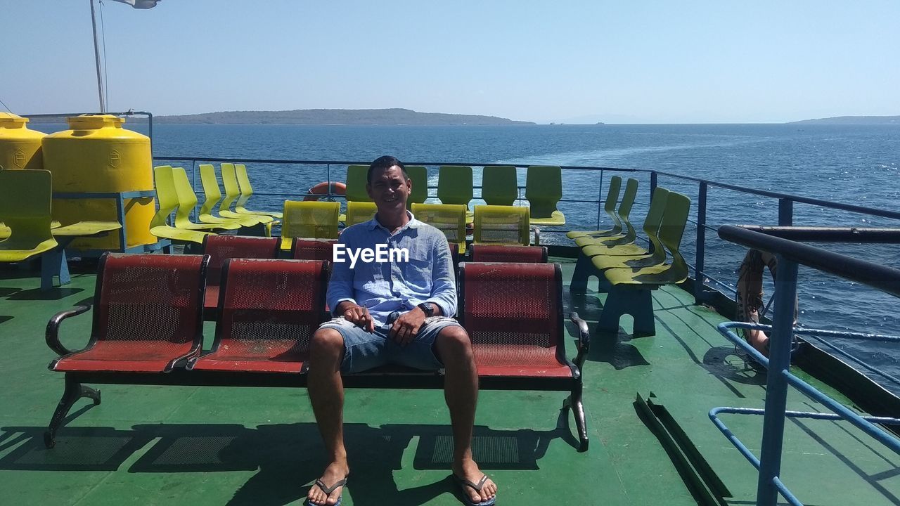 FULL LENGTH OF MAN SITTING ON SEAT AT SEA