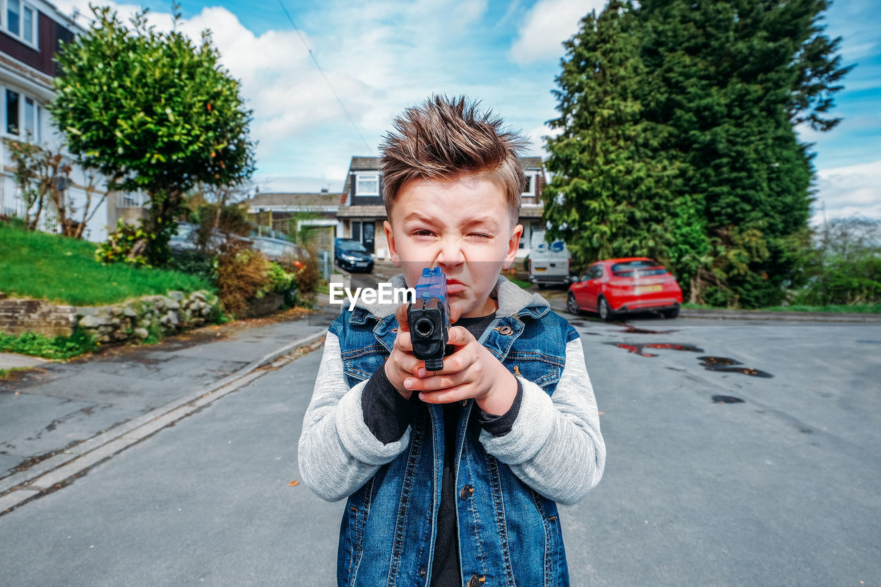 Portrait of boy shooting with toy handgun while standing on road