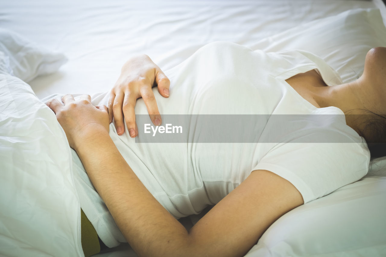 Midsection of woman with stomachache lying on bed at home