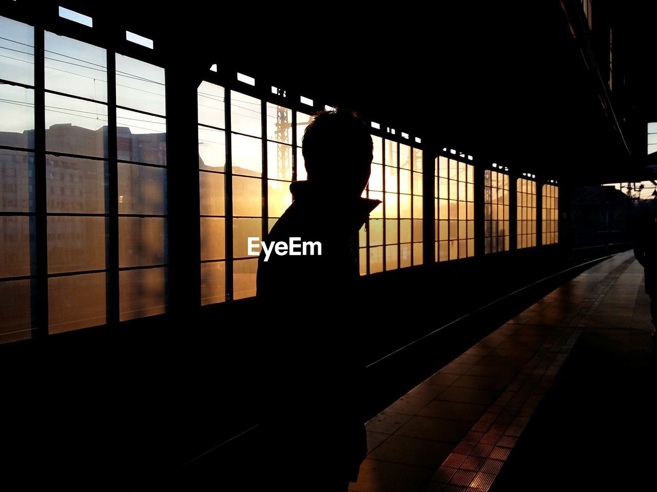 Silhouette man standing in railroad station during sunset