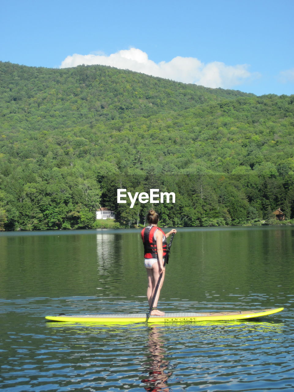 Full length of woman paddleboarding on river by tree mountain against sky