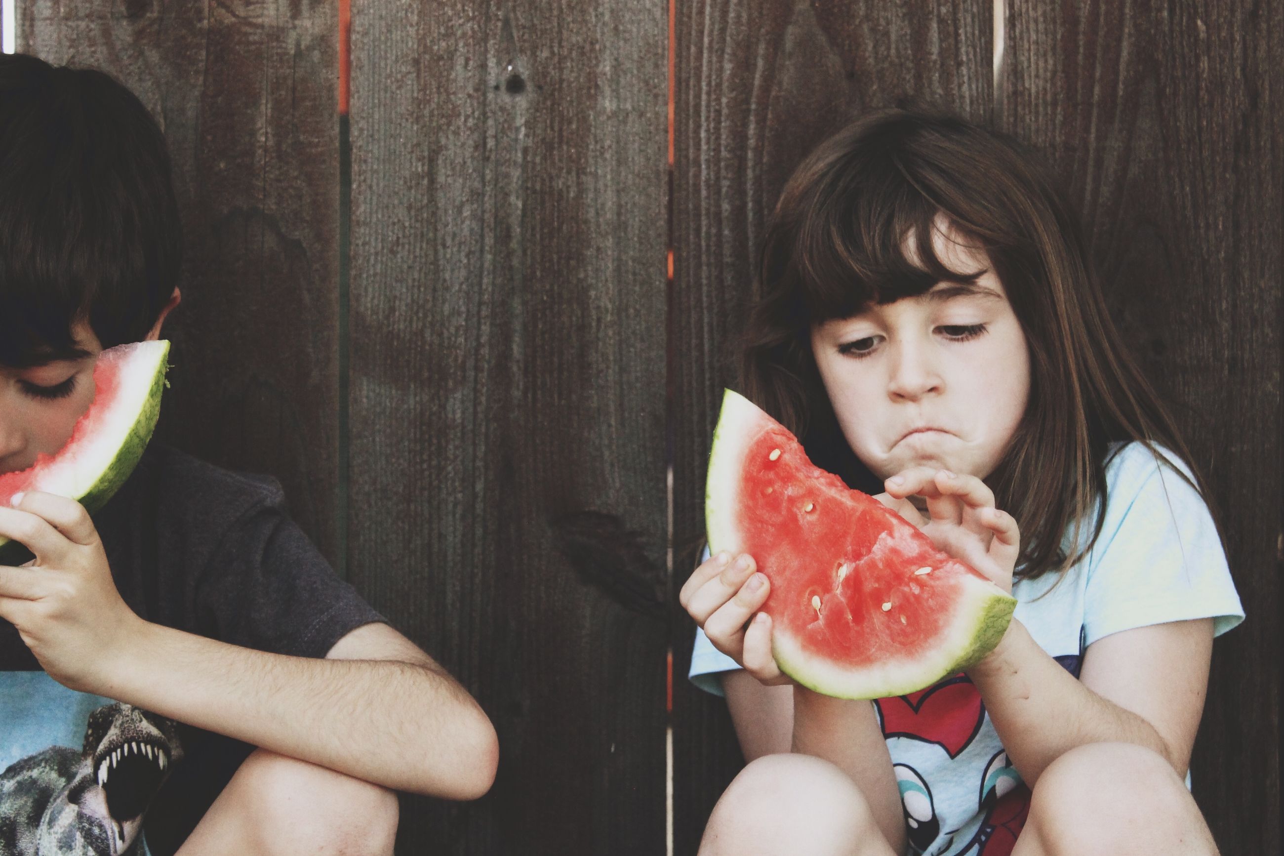 Siblings eating watermelon against wooden | ID: 117457599