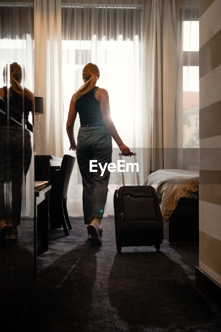 Woman traveler with luggage suitcase after checking into a hotel room looking in the window