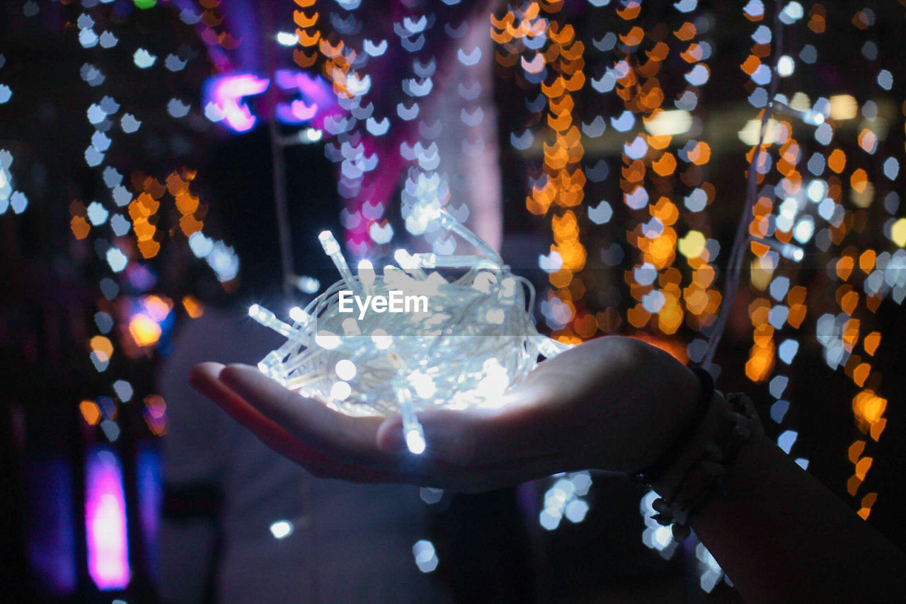 Close-up cropped hand holding of illuminated christmas lights
