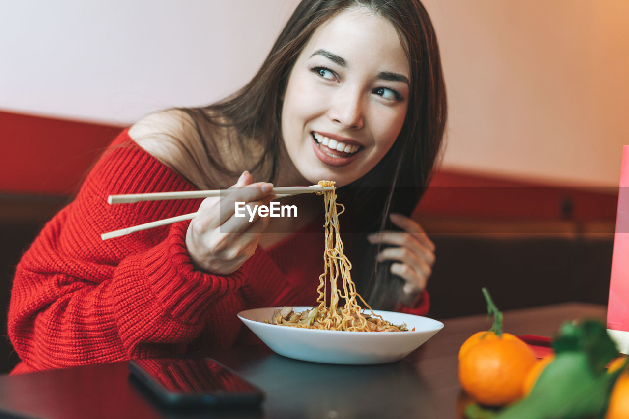 Beautiful asian woman in red clothes eating asian food with chopsticks in chinese restaurant