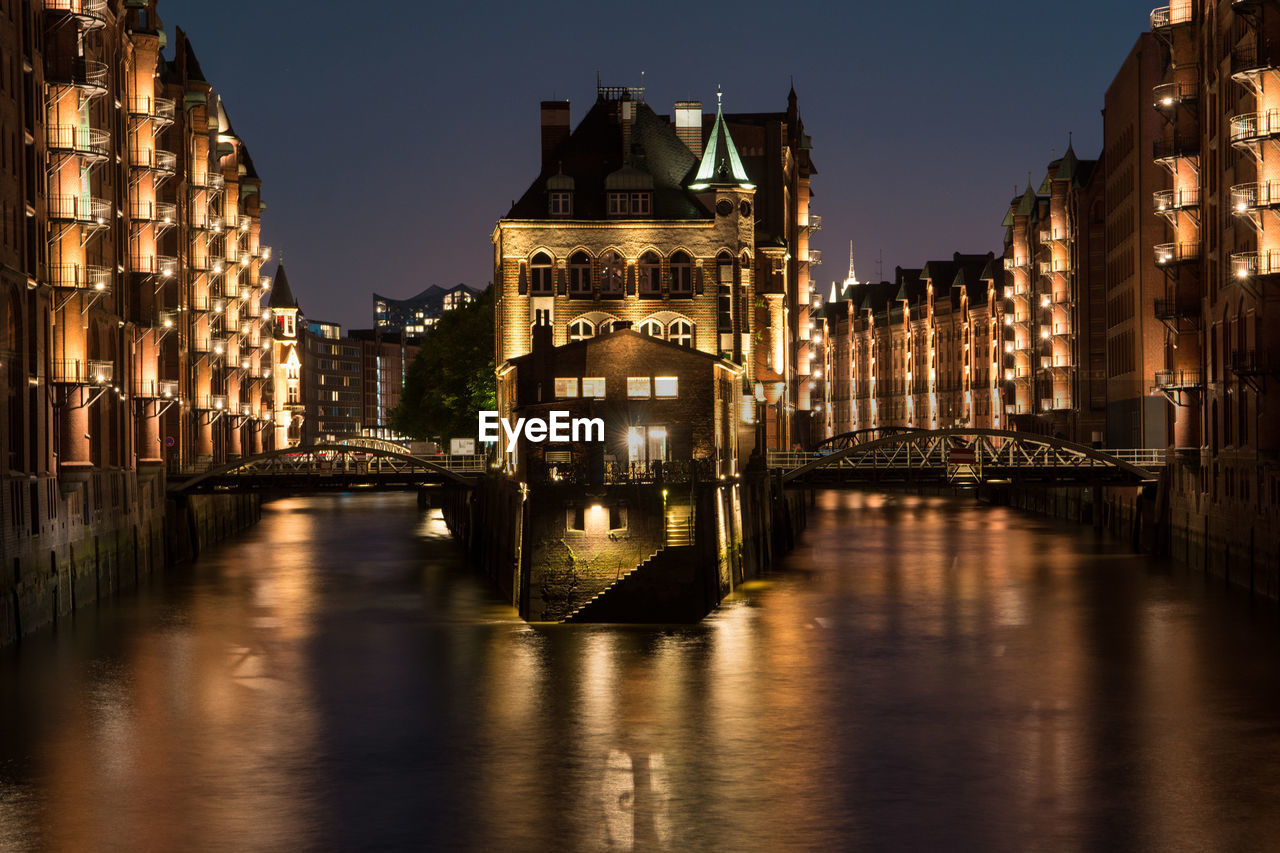 Bridge over river amidst buildings in city at night