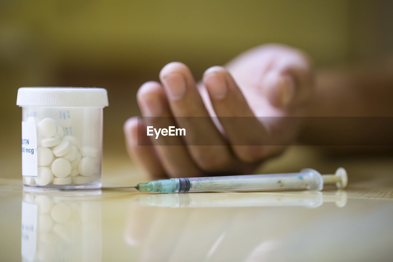 Close-up of human hand by pill bottle and syringe