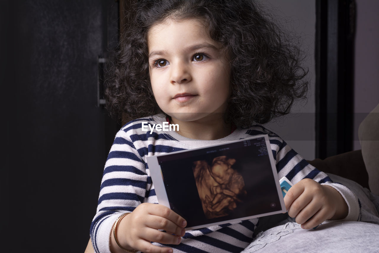 Cute girl holding ultrasound photograph at home