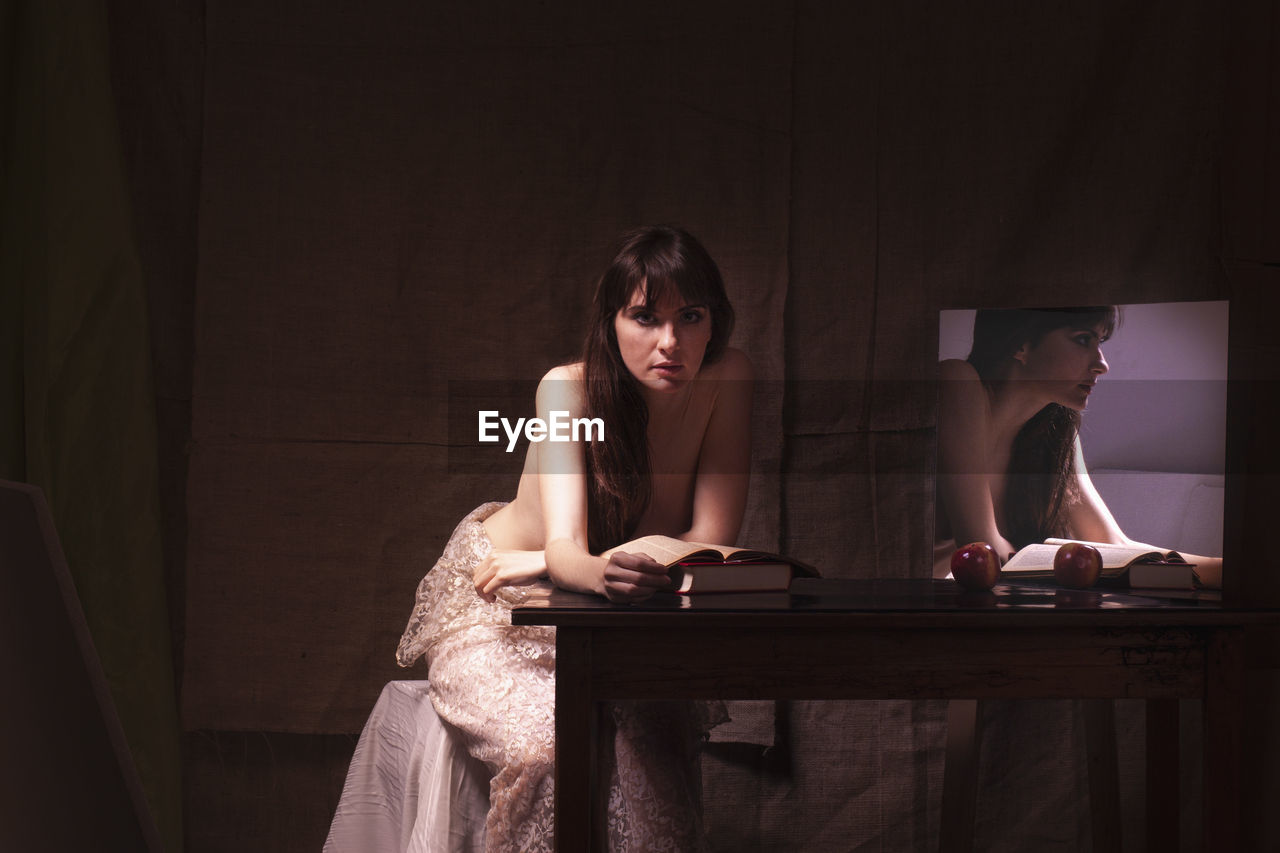 Portrait of shirtless young woman sitting on table with mirror