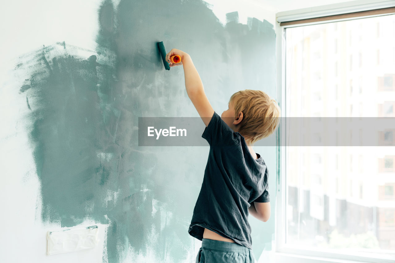 Rear view of boy painting on wall at home