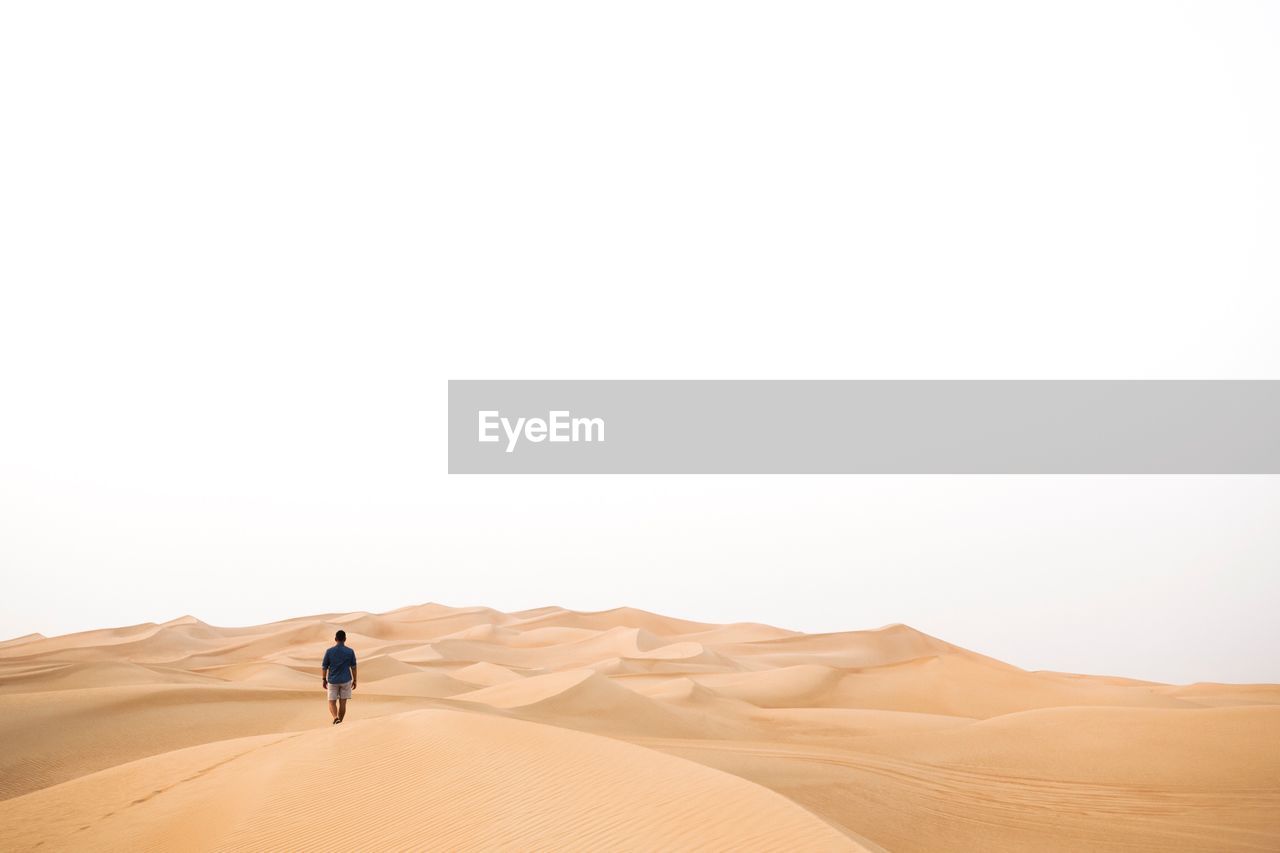 Rear view of man walking at desert against clear sky
