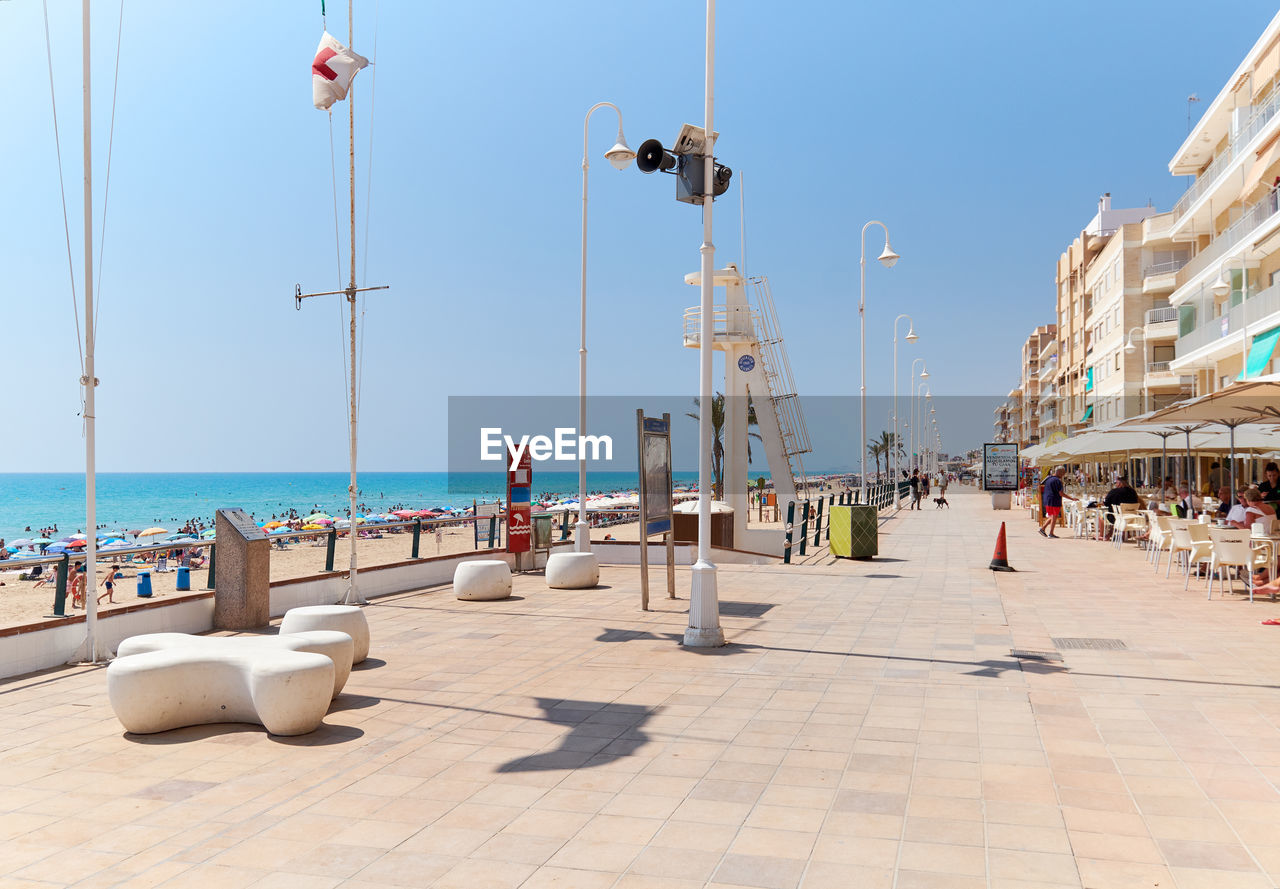 People at beach in city against clear sky