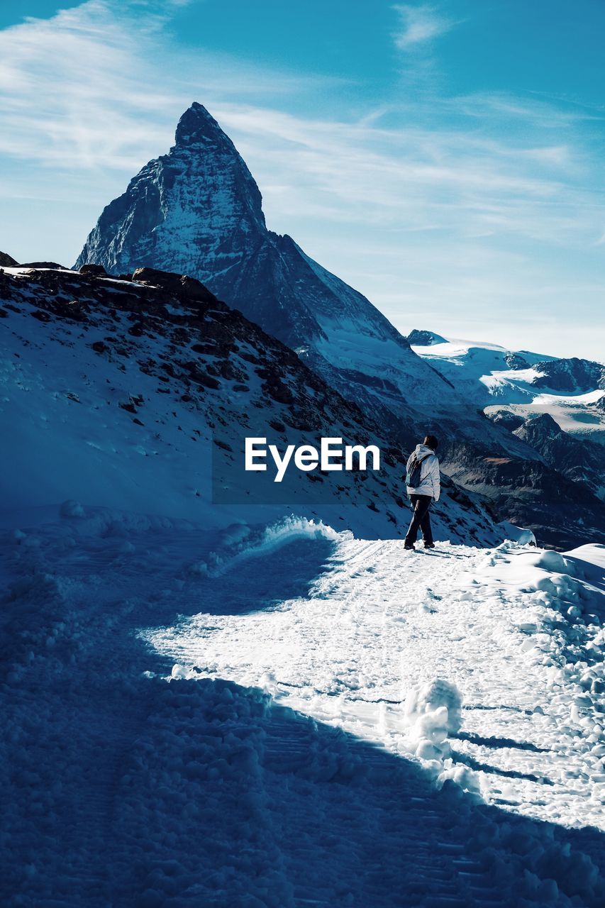 Man walking on snow covered mountain against sky