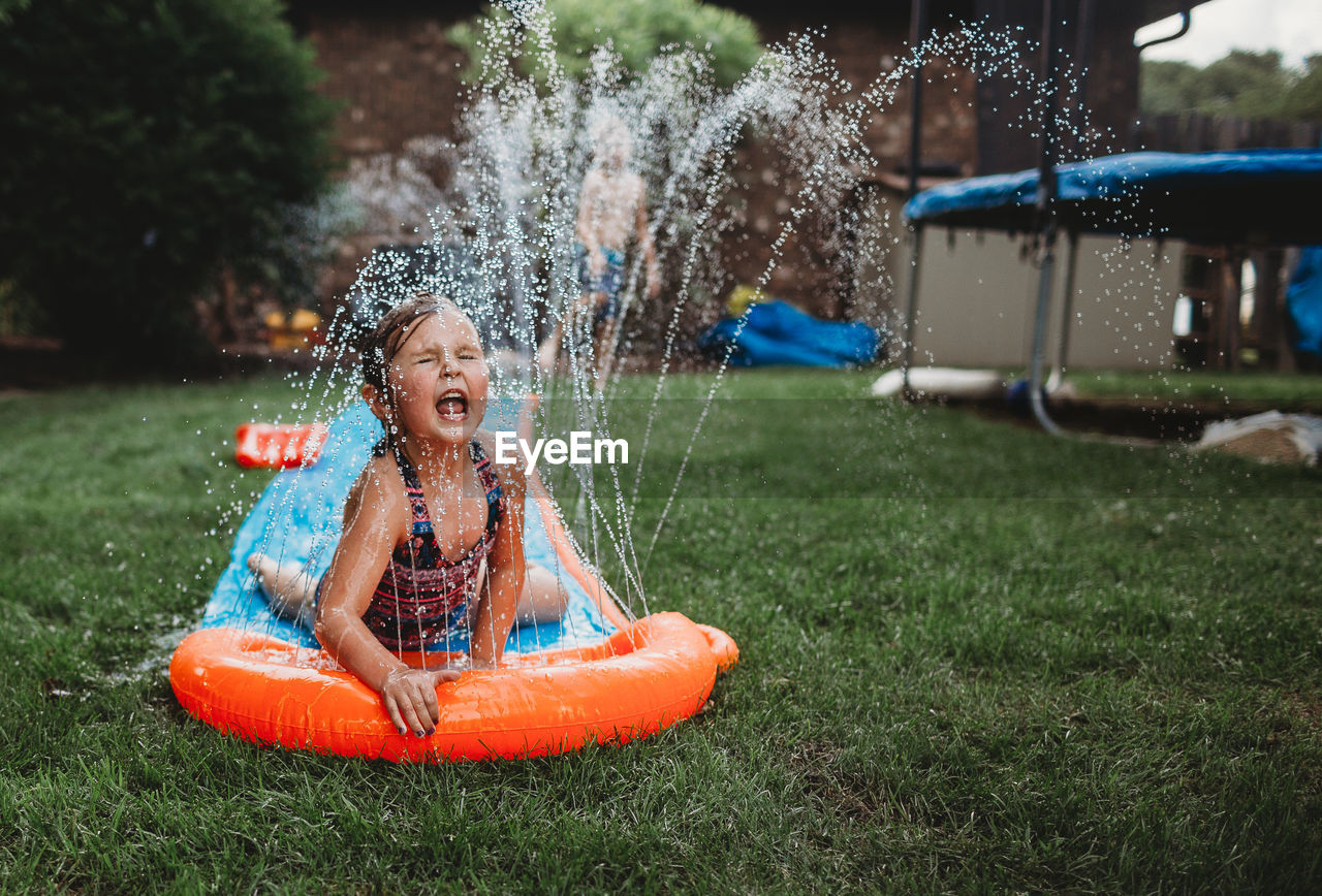 Girl playing on water slide over field