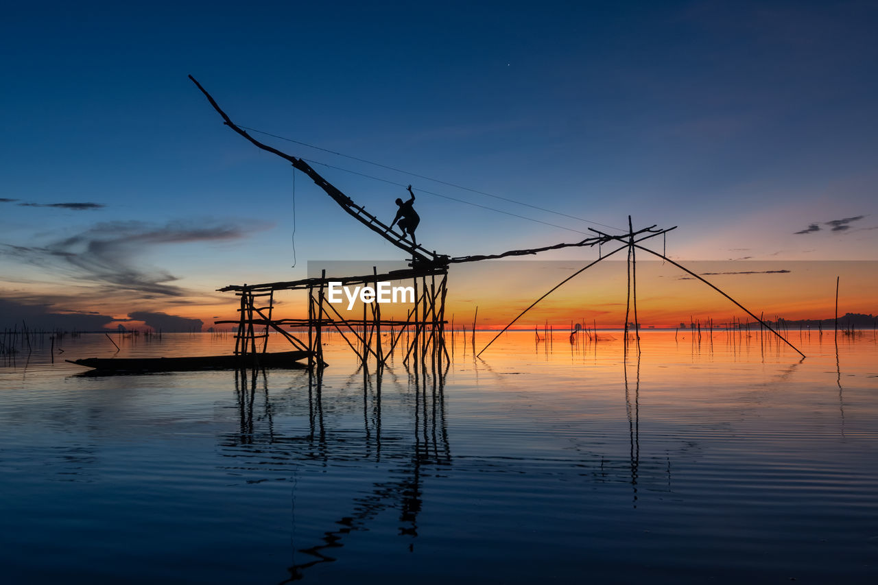 Silhouette fisherman on built structure in sea during sunset