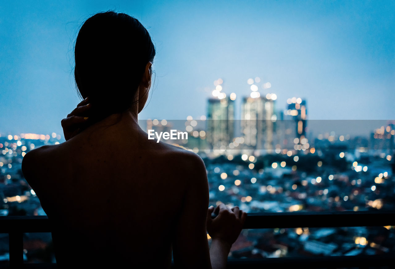Rear view of shirtless woman looking at cityscape against sky