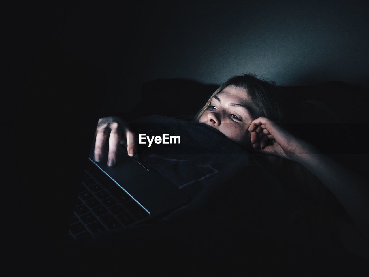 Young woman using laptop while lying on bed in darkroom