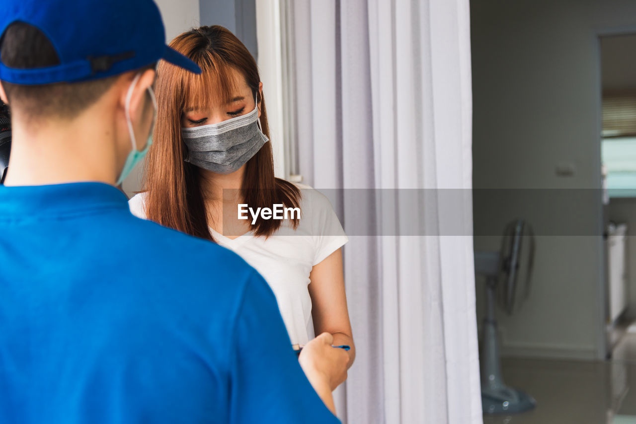 Young woman wearing mask taking delivery standing at door