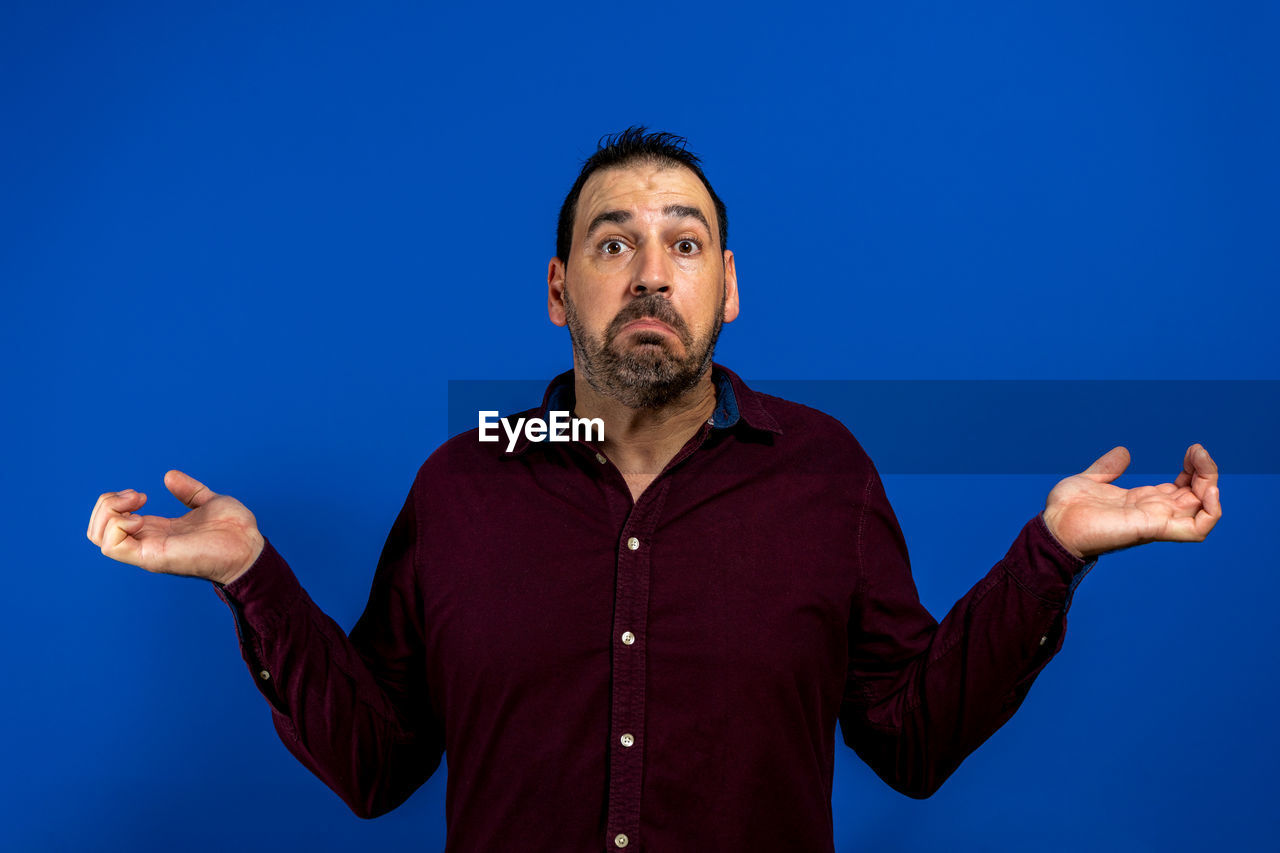 MAN LOOKING AT CAMERA AGAINST BLUE BACKGROUND