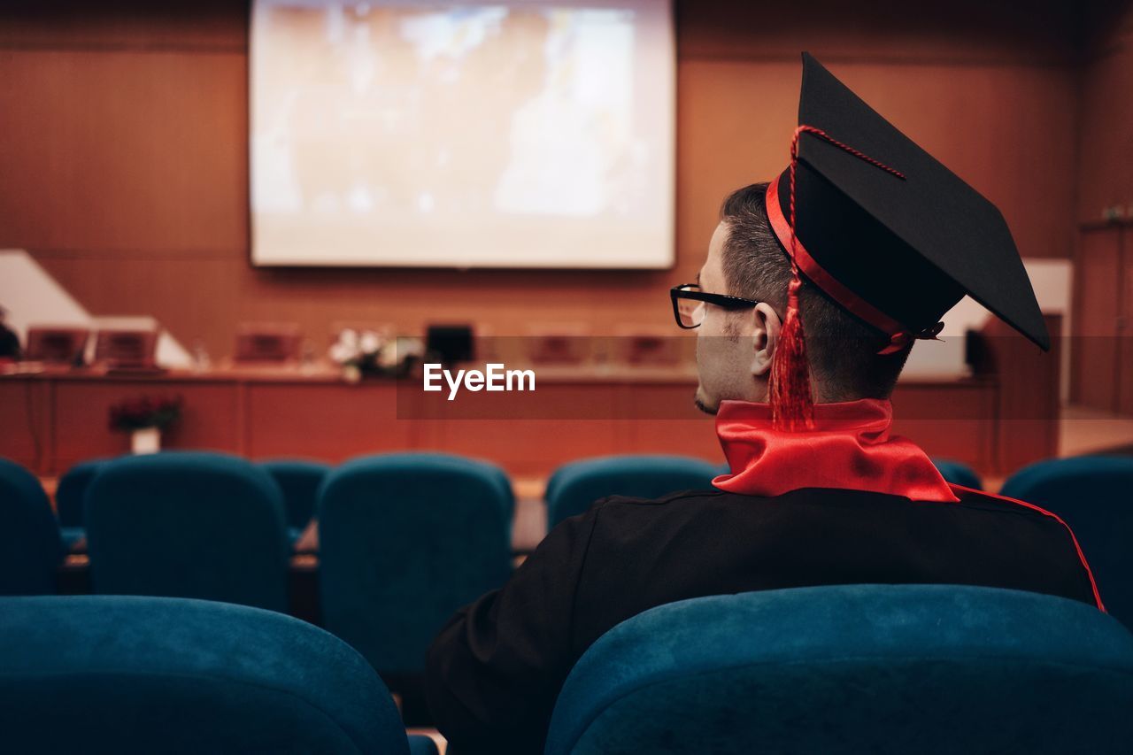 Man wearing mortarboard while sitting in lecture hall
