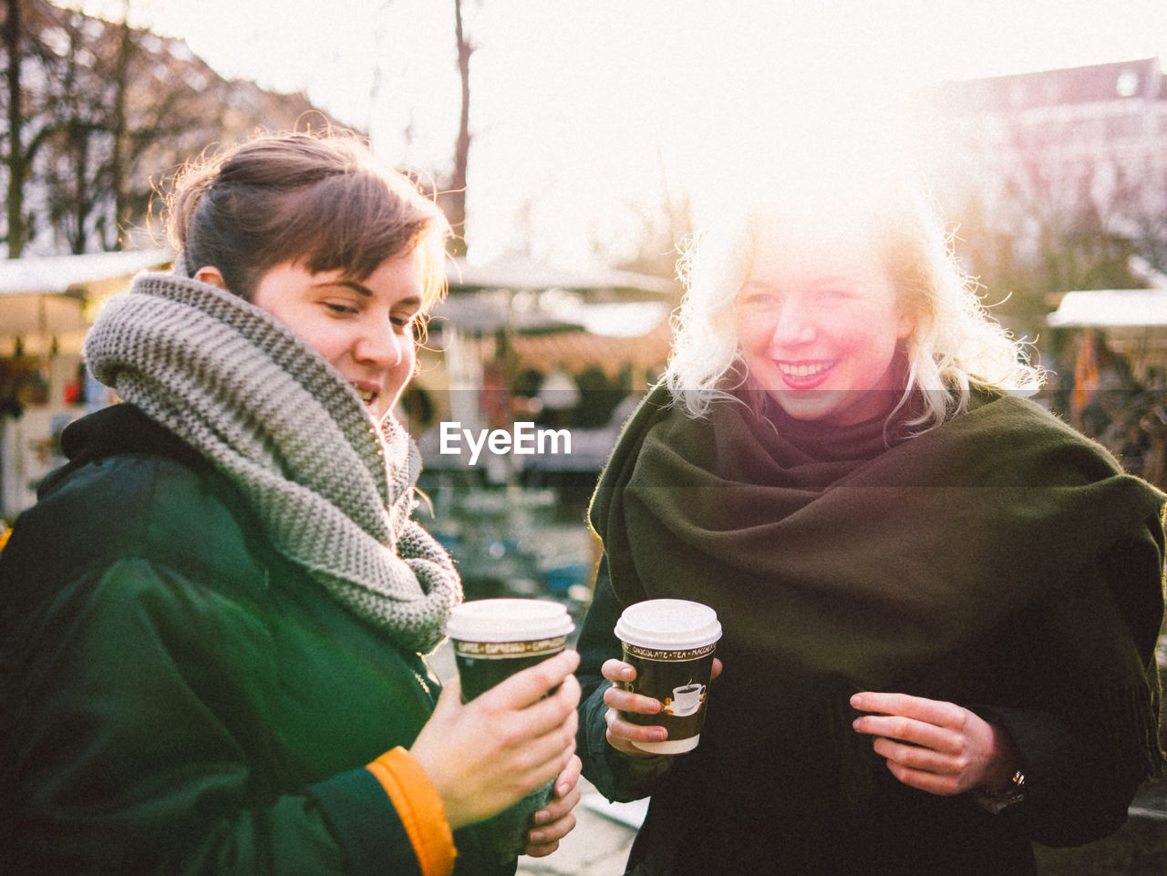 Happy friends holding disposable coffee cup in flea market