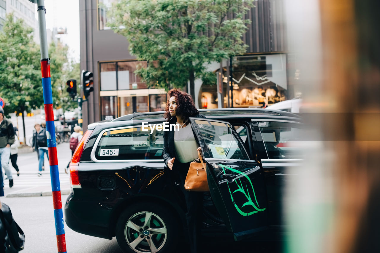 Mid adult businesswoman disembarking from taxi on street in city