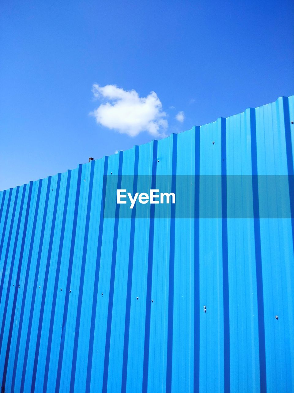 LOW ANGLE VIEW OF METALLIC STRUCTURE AGAINST BLUE SKY AND FENCE