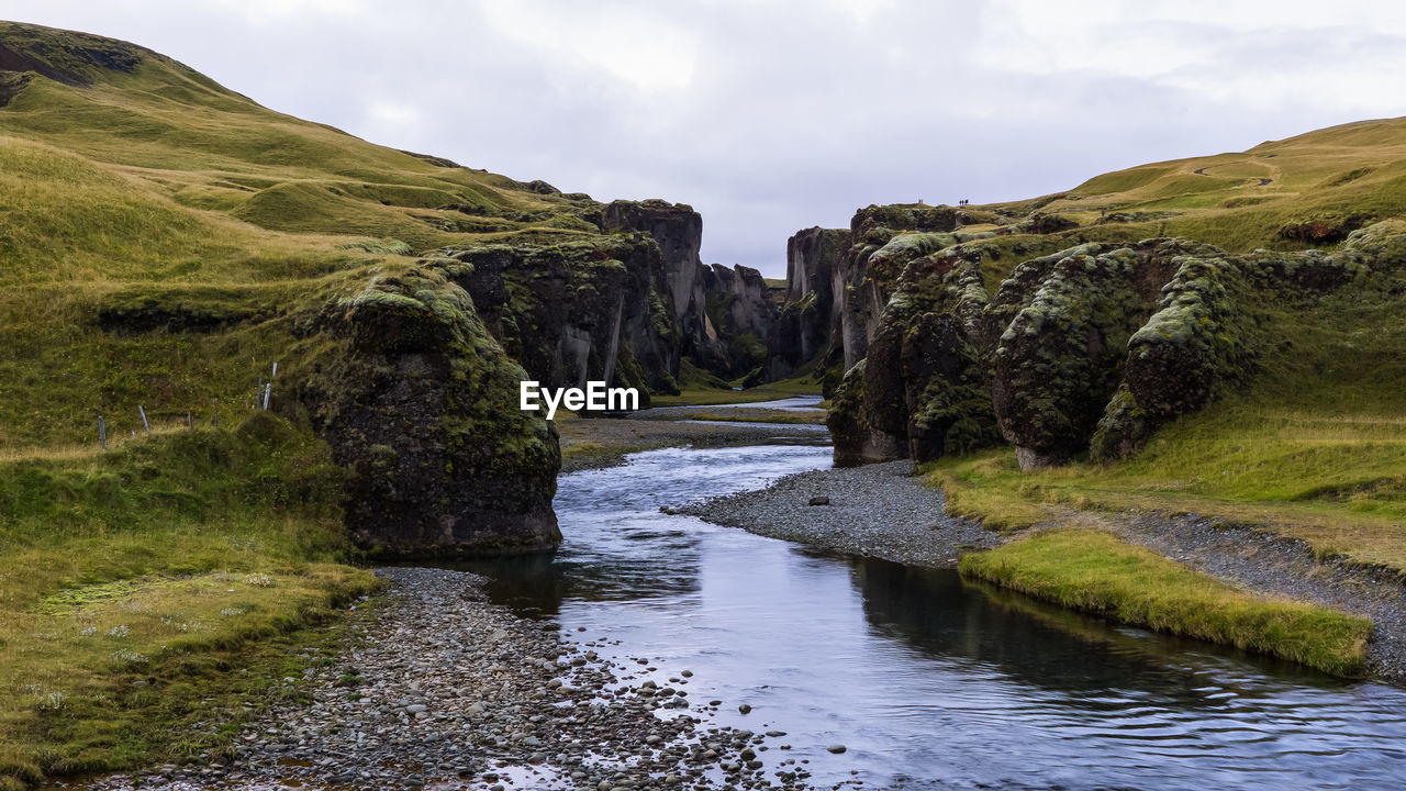 Stream amidst cliff against sky