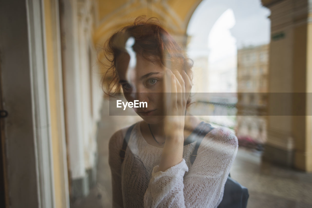PORTRAIT OF YOUNG WOMAN LOOKING THROUGH WINDOW