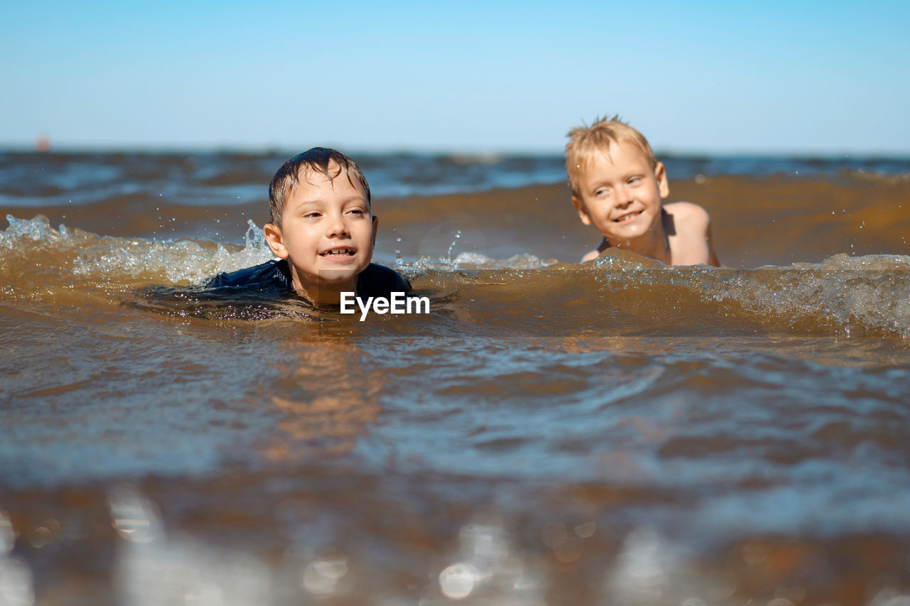7-8 years old cute caucasian boys swimming in the sea with big splashes in waves