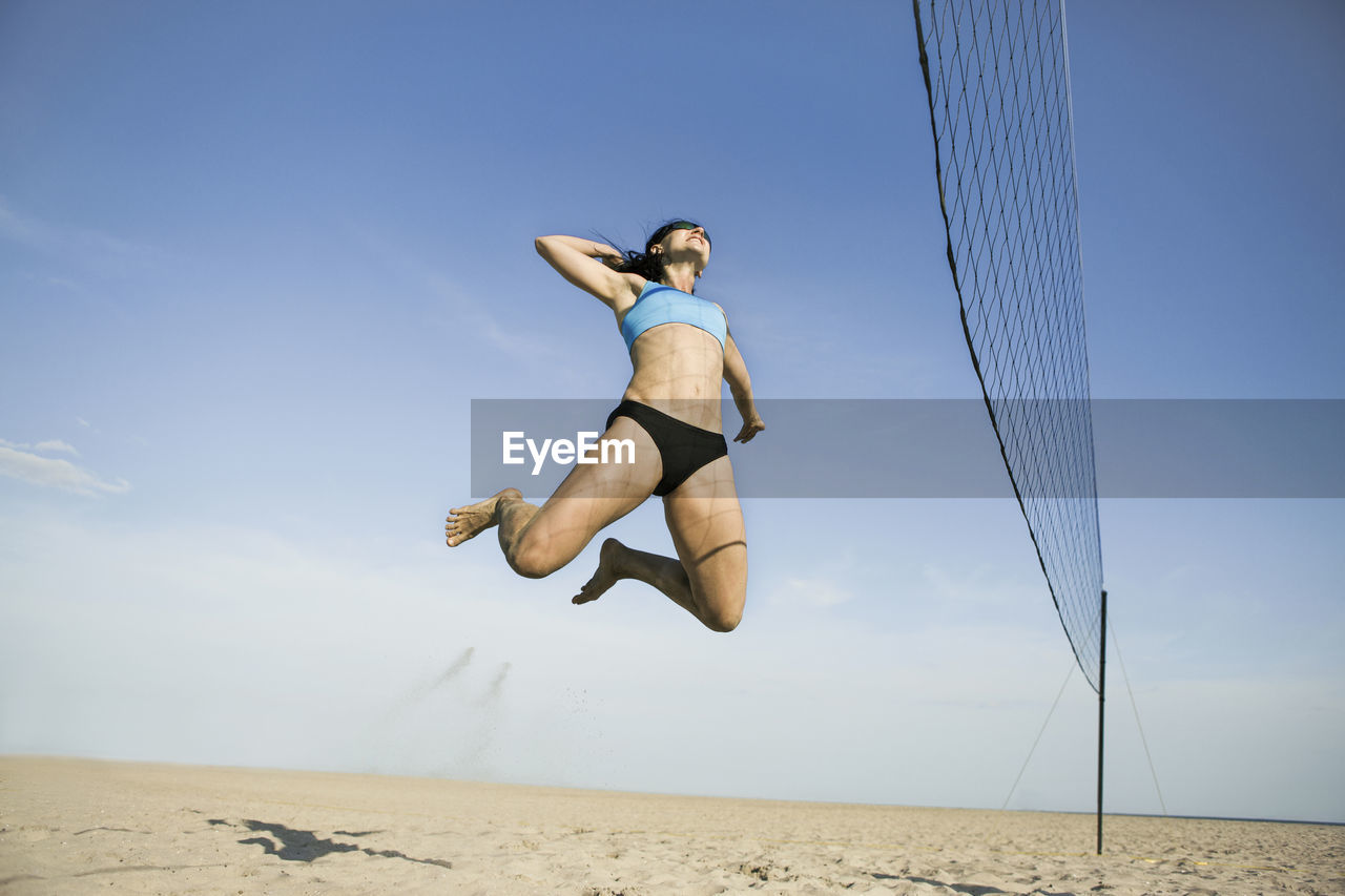Low angle view of woman jumping while playing volleyball at beach