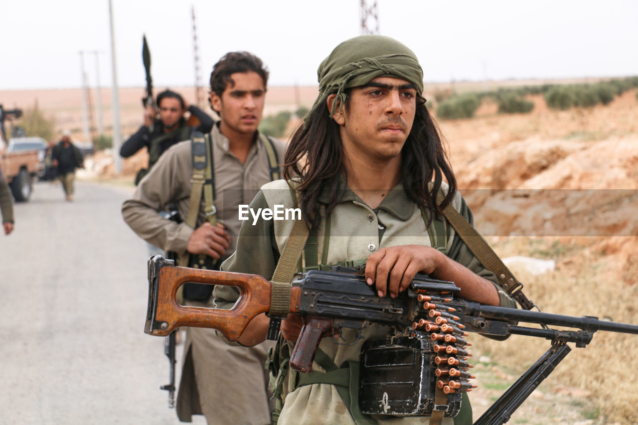 People with rifles and ammunition walking on road