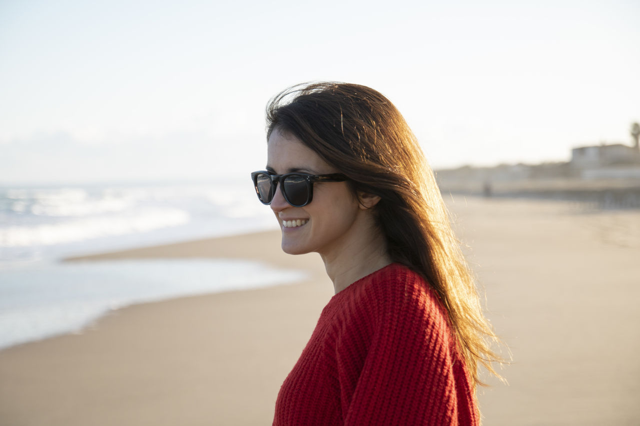 Side view of woman wearing sunglasses standing at beach
