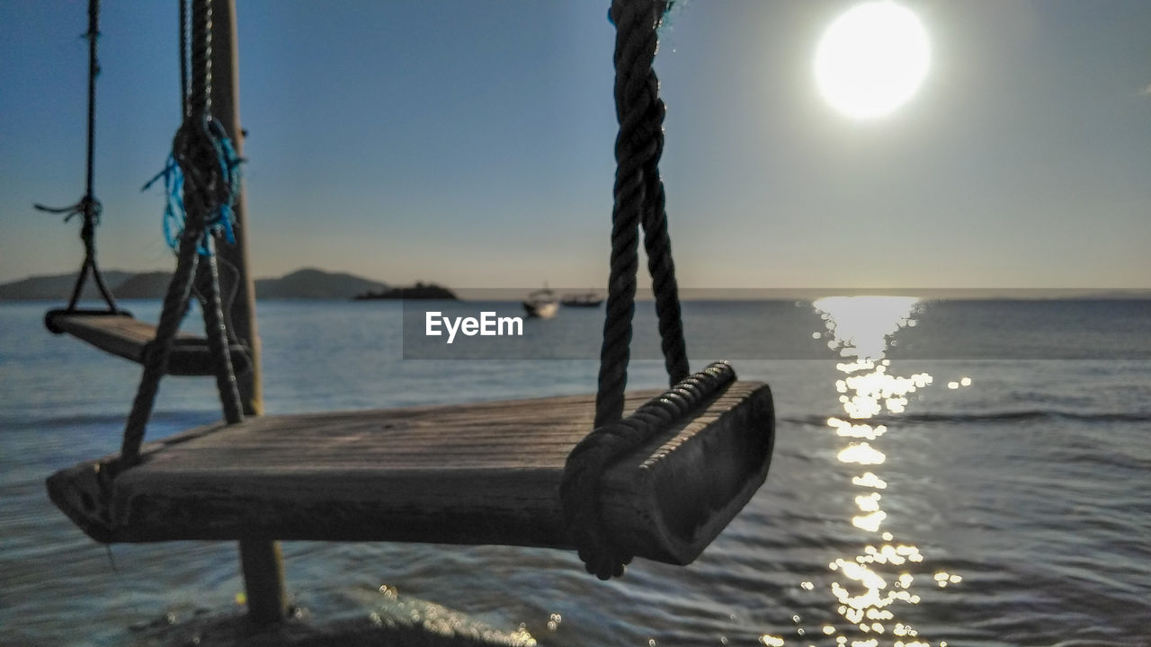 Close-up of swing by sea against sky during sunset