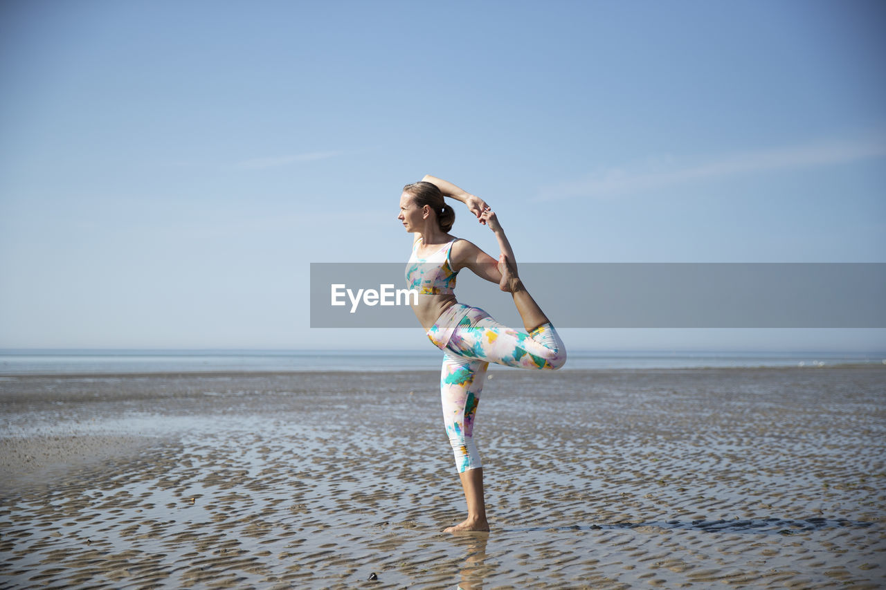 side view of woman jumping on beach against clear sky