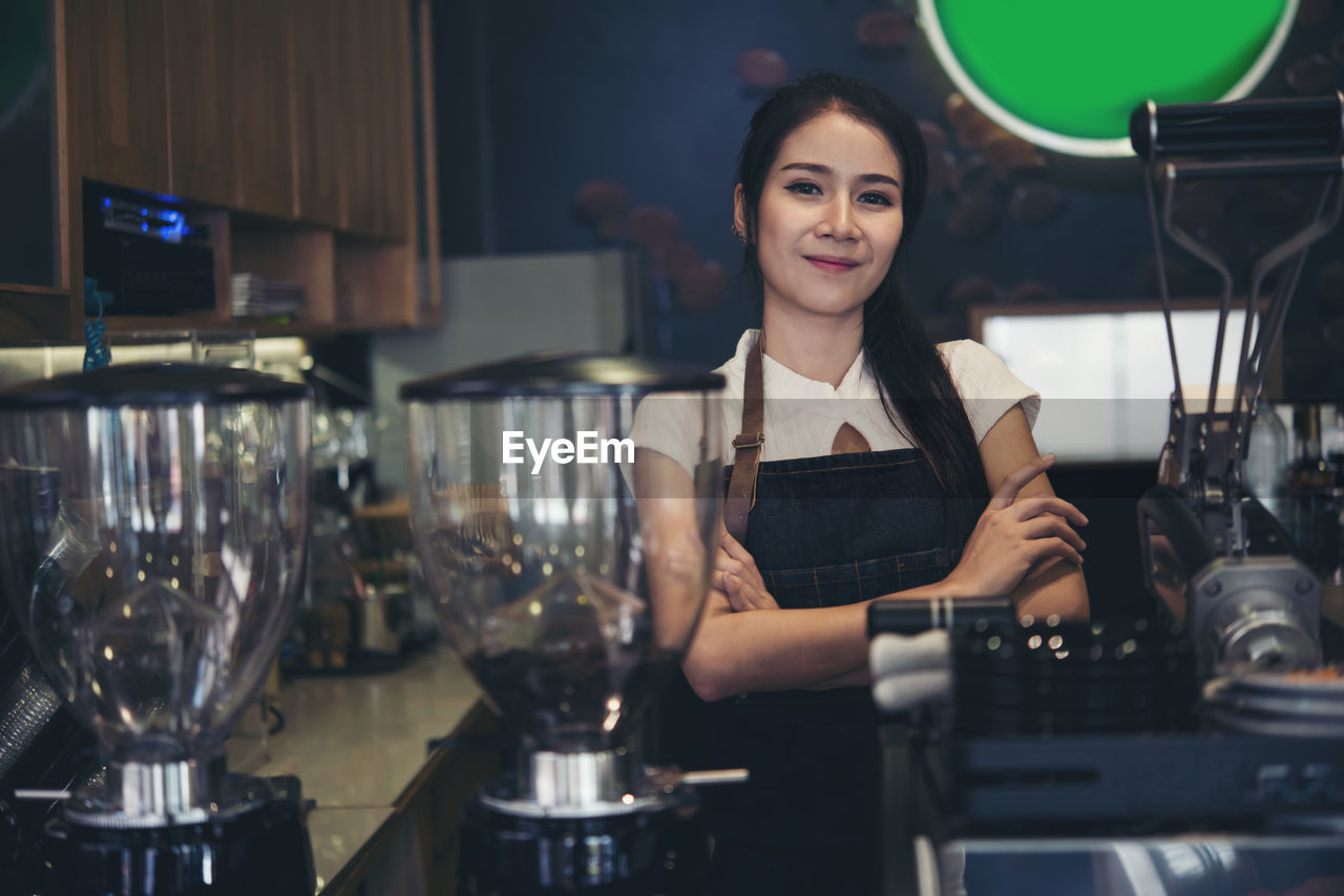 PORTRAIT OF SMILING WOMAN STANDING IN KITCHEN