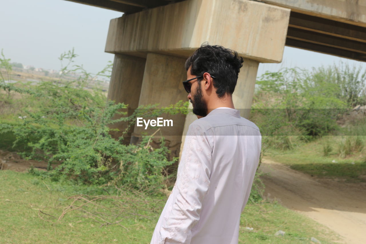 one person, men, adult, young adult, nature, plant, architecture, lifestyles, standing, day, waist up, built structure, leisure activity, outdoors, casual clothing, tree, beard, looking, side view, contemplation, ceremony, facial hair, grass, land