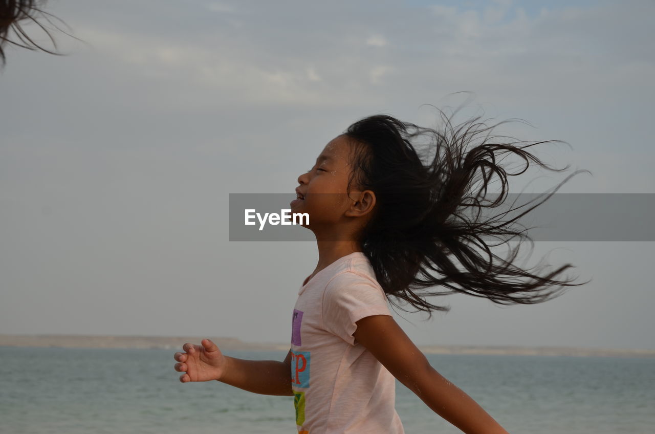 Side view of happy girl on beach against sky