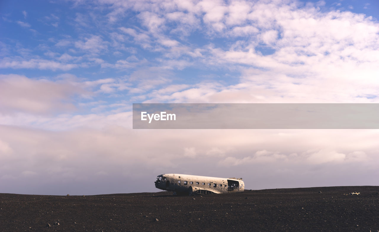 Crashed airplane on landscape against clouds