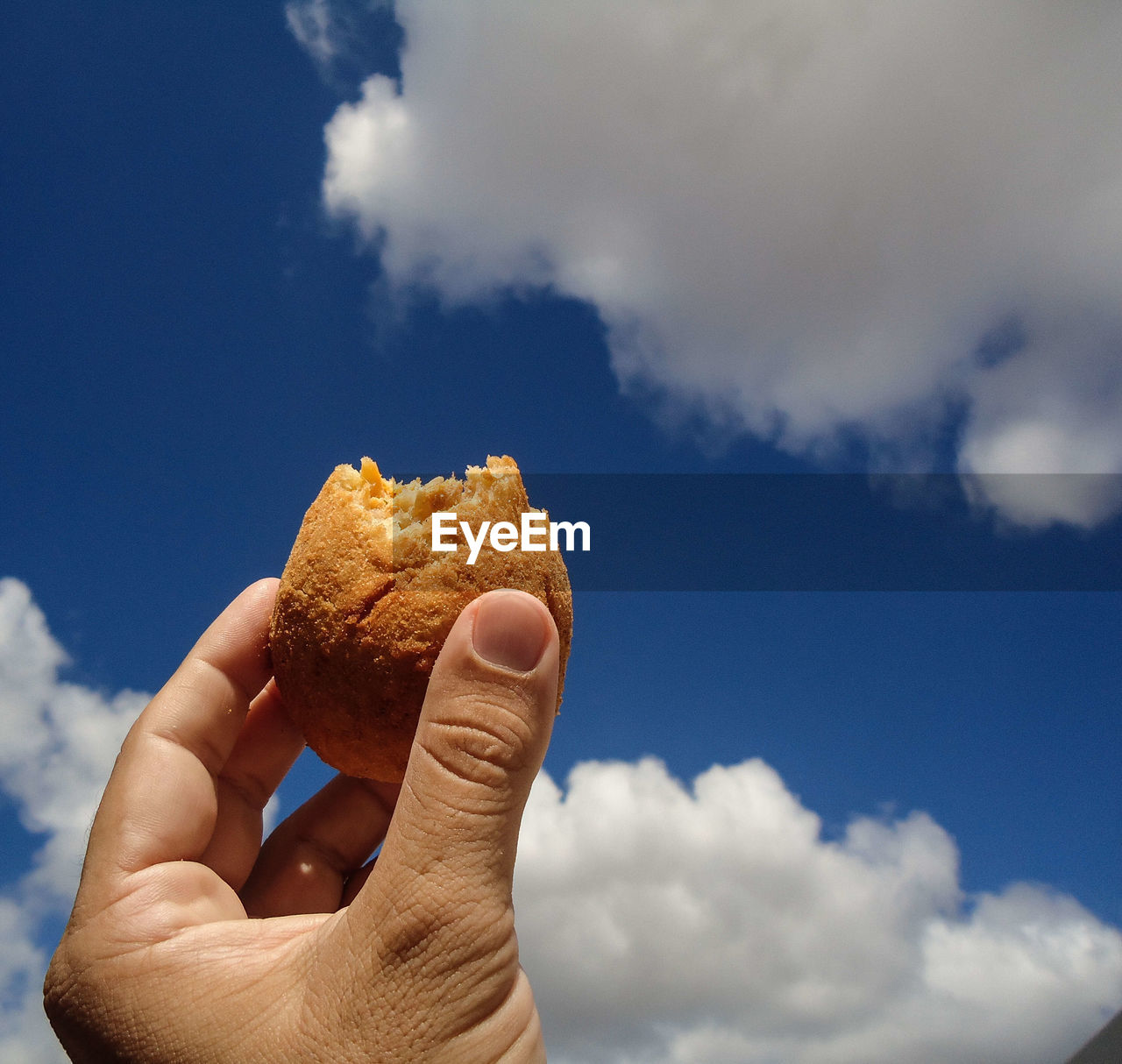 A hand holding a drumstick with sky in the background