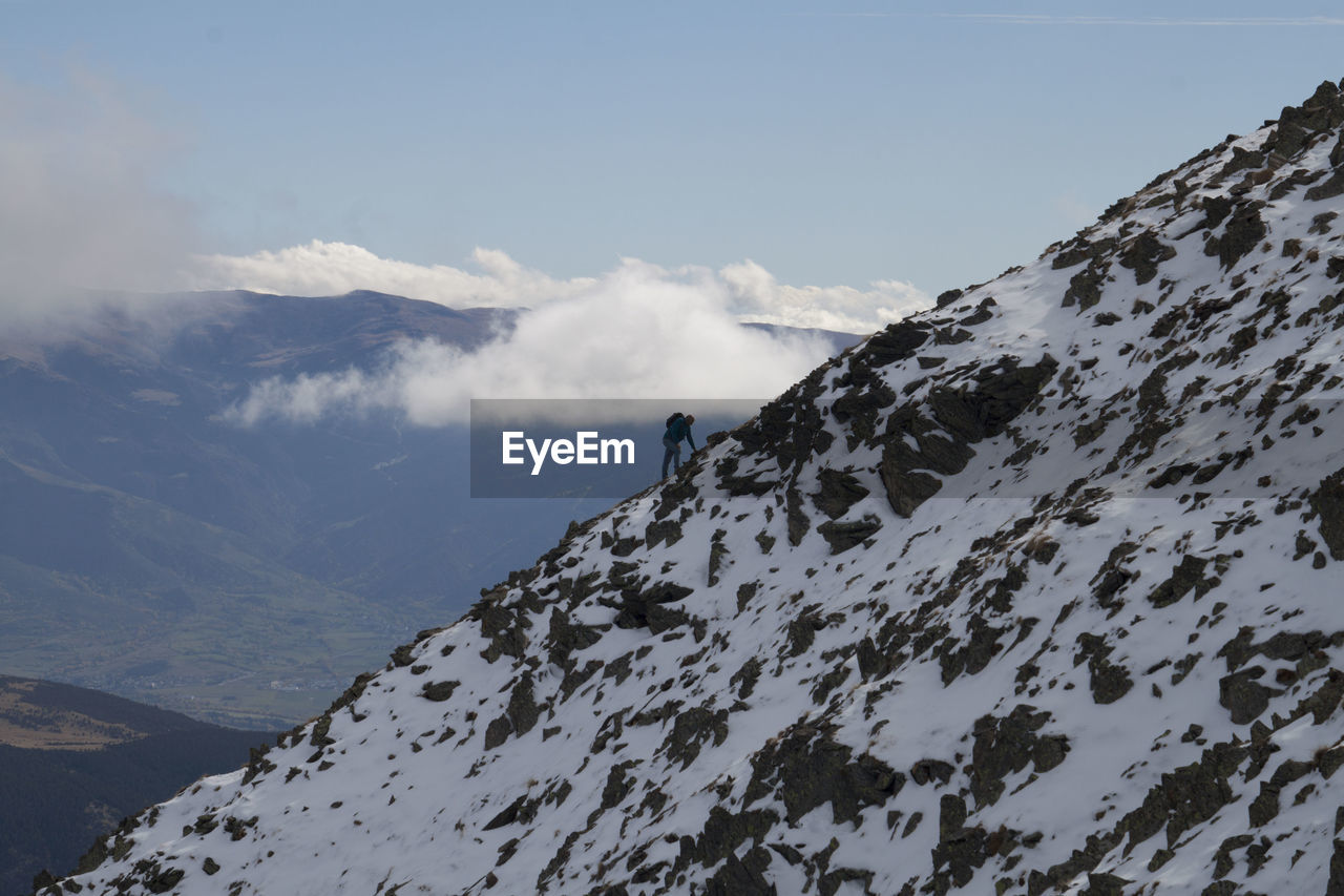 Man climbing on snowcapped mountains against sky