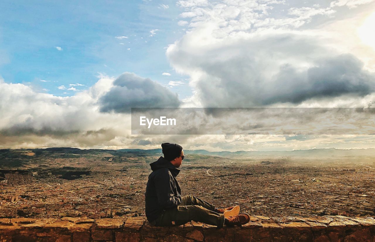 Side view of man sitting on rock against sky