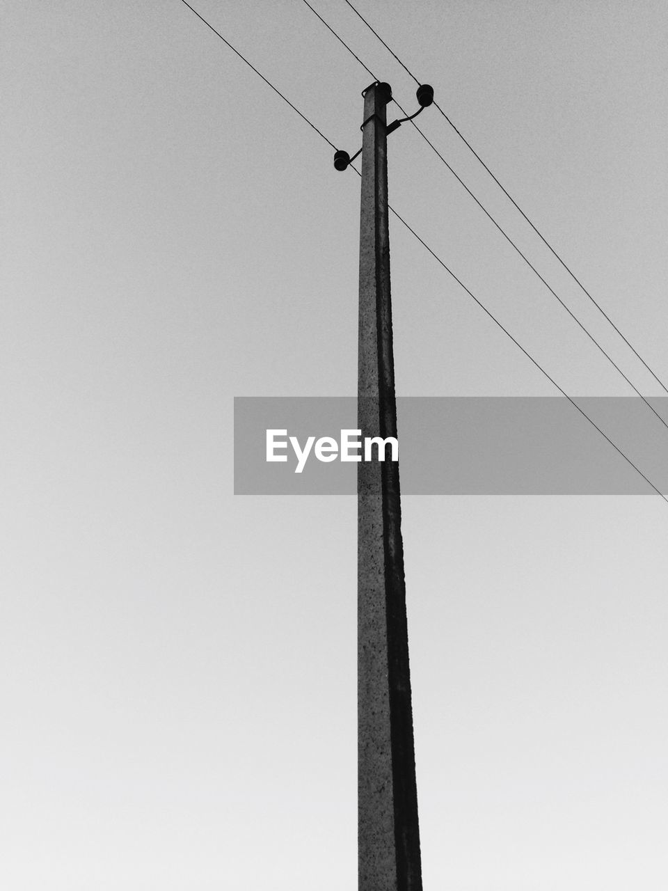 Low angle view of power lines with pole against clear sky